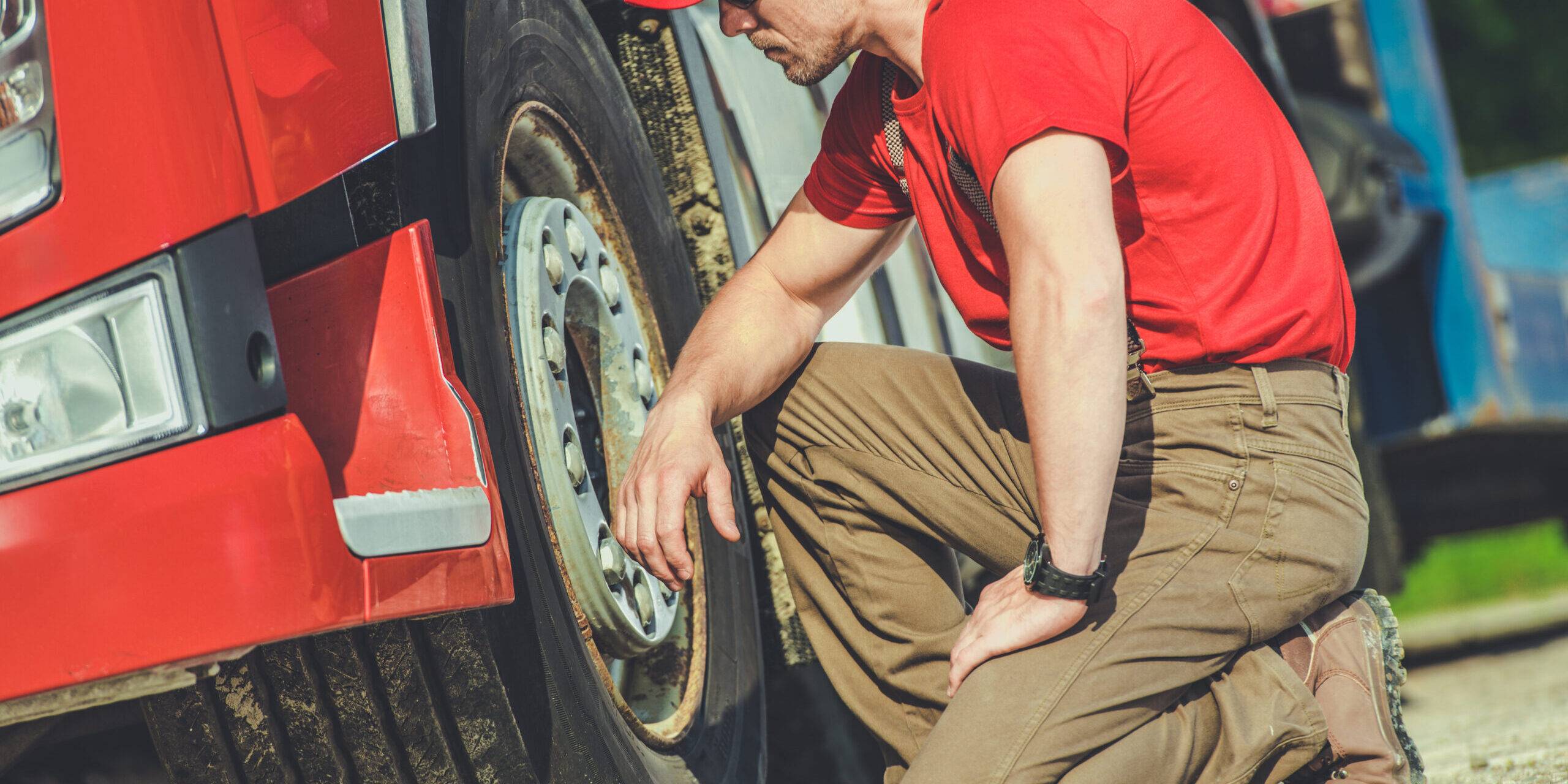 Truck Mechanic Inspecting Tire Of A Red Truck On A Sunny Day In A Service Area Truck Mechanic Inspecting Tire Of A Red Truck On A Sunny Day In A Service Area